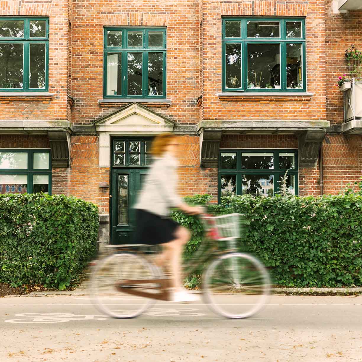 Cyklist passerer klassisk murstensbygning med grønne vinduer i roligt bymiljø