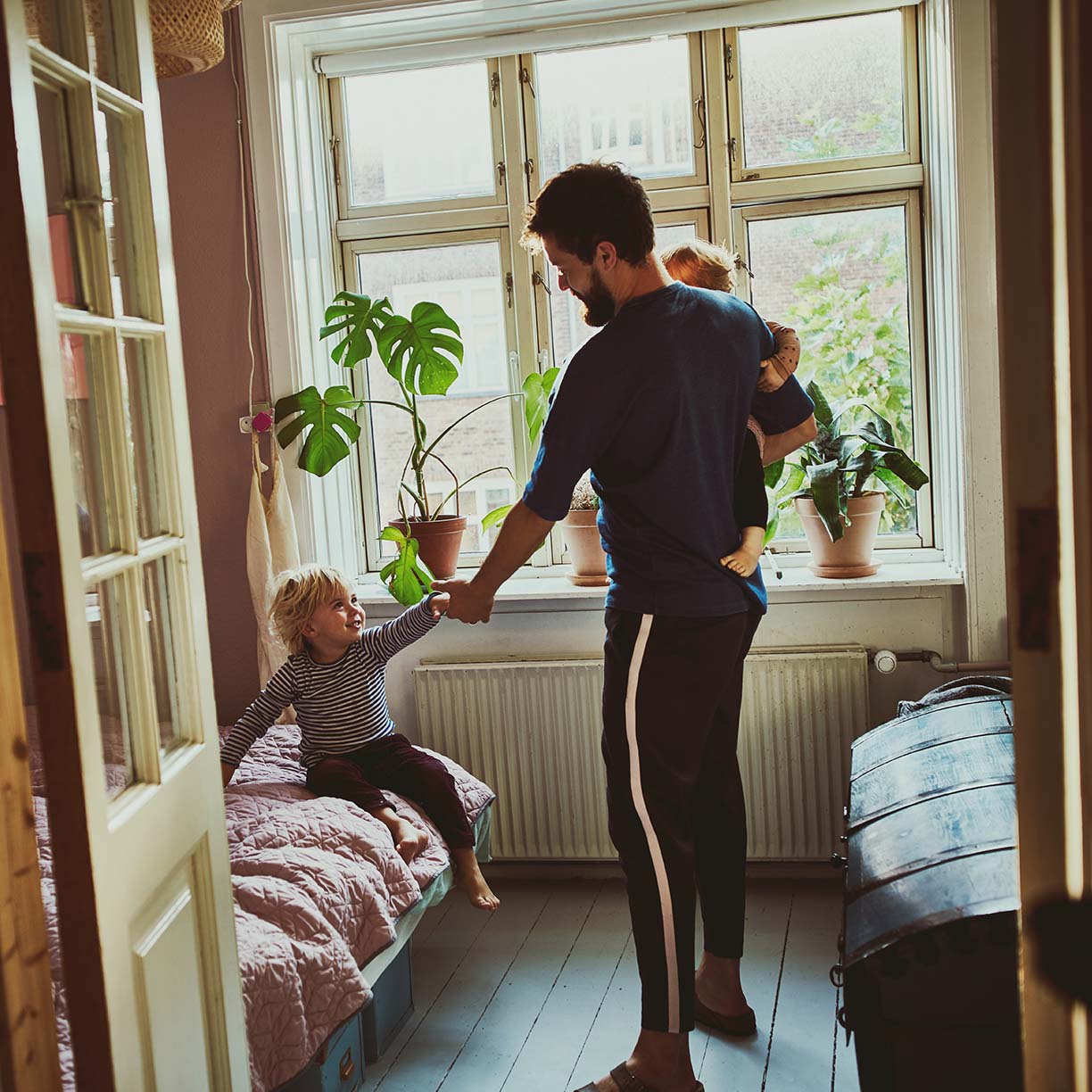 Far leger med sine børn i soveværelse i hjemmet med dagslys og stueplanter