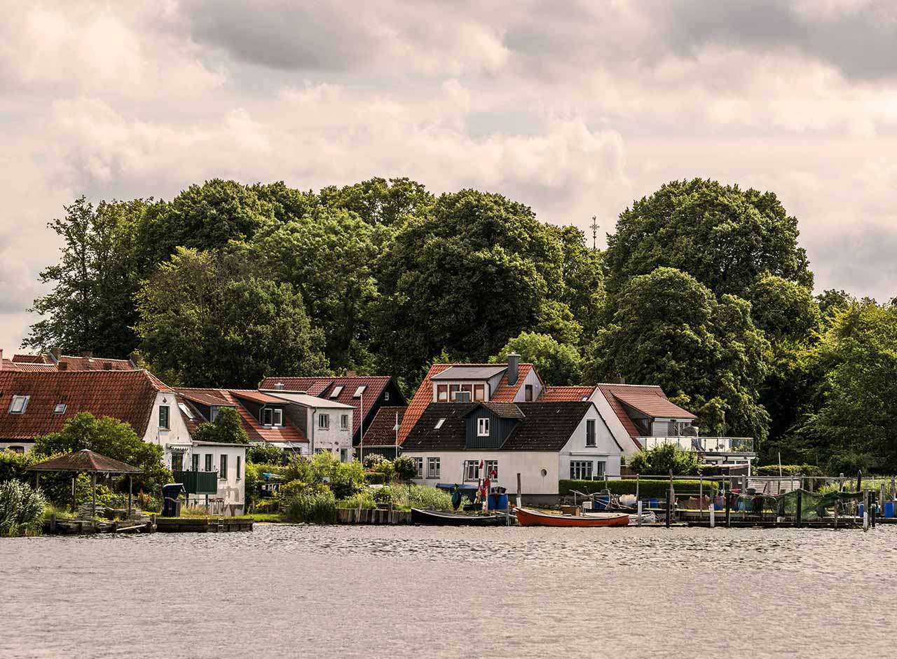 Danske huse ved vandet i en grøn kystby med bådebro og udsigt over fjord, attraktivt boligområde tæt på natur