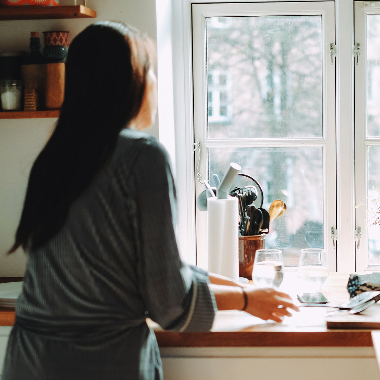 Kvinde står ved køkkenvindue i lejlighed med planter og dagslys
