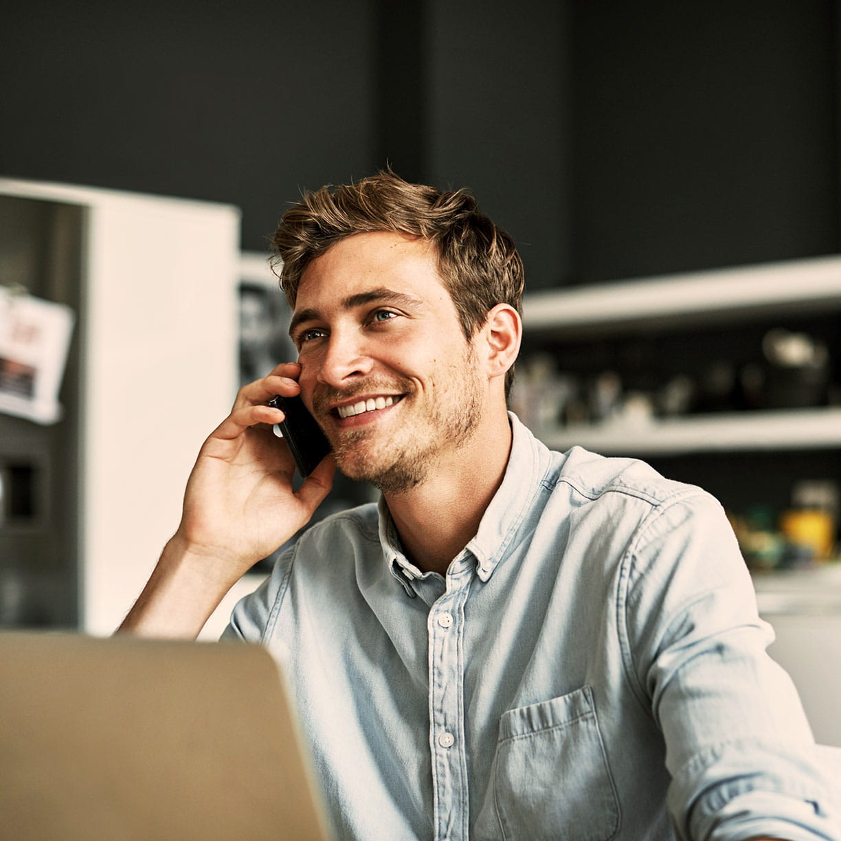 Mand arbejder hjemme ved laptop og taler i telefon i køkkenalrum