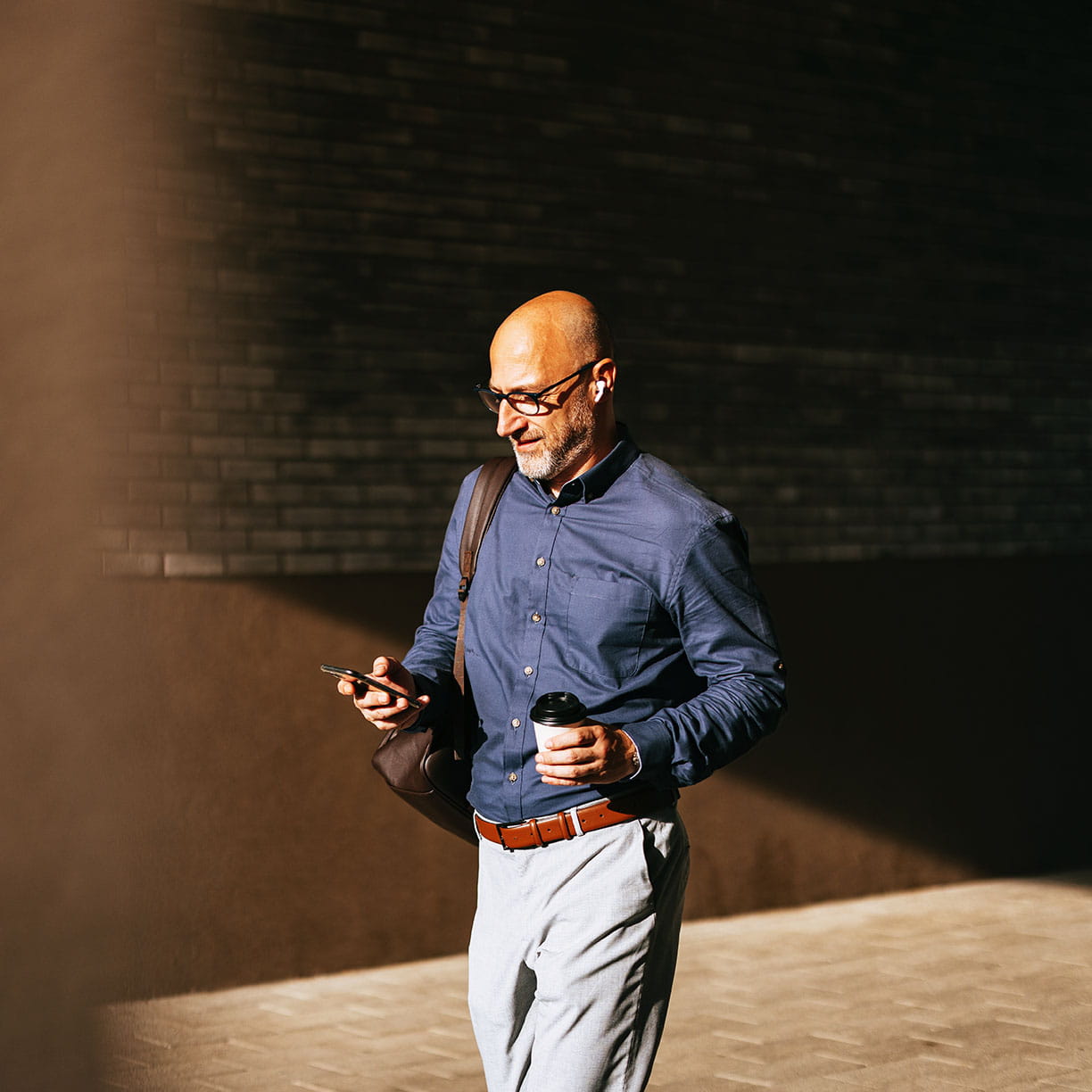Mand i skjorte og briller går gennem et urbant byrum med kaffekop i hånden