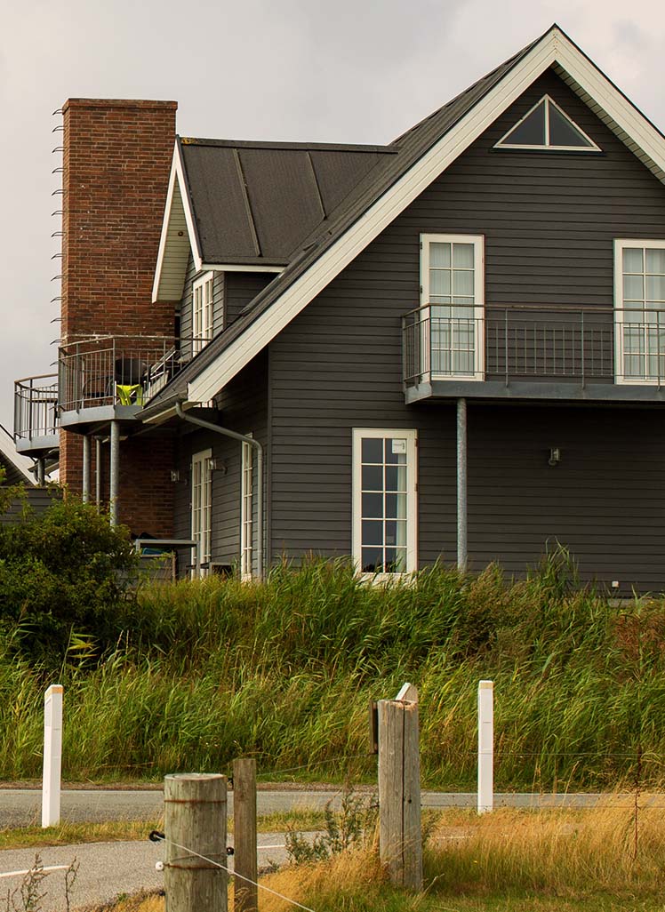 Moderne sommerhuse med mørke træfacader og saddeltag placeret i kystnært område med grønne klitter og vej i forgrunden