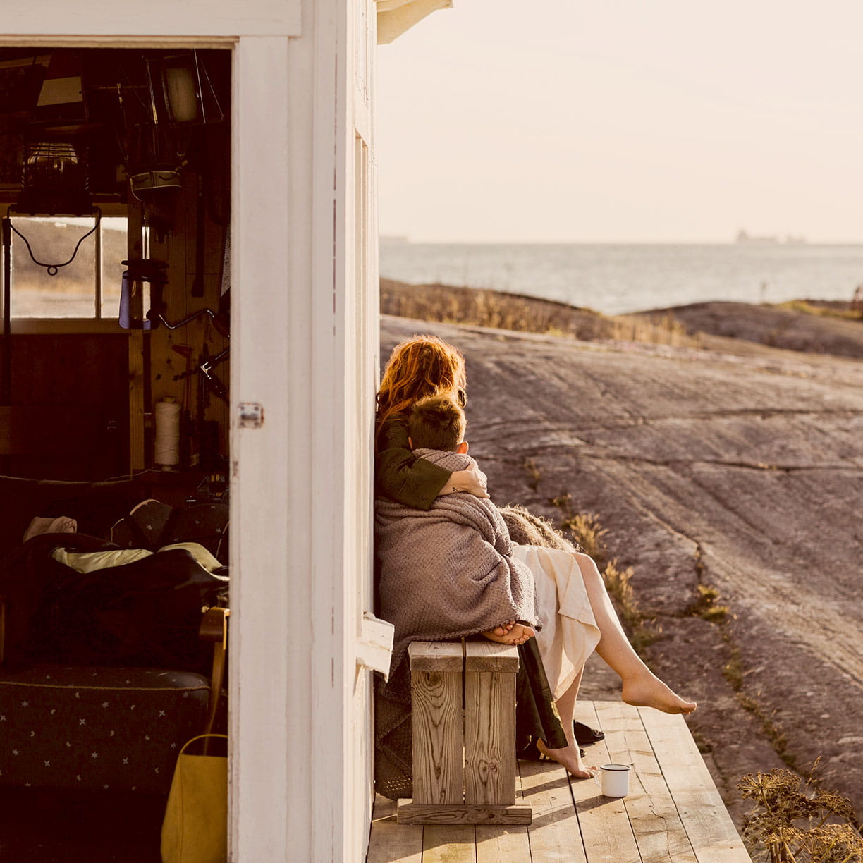 Et par sidder tæt sammen på en terrasse ved kysten og nyder udsigten over havet i aftensolen