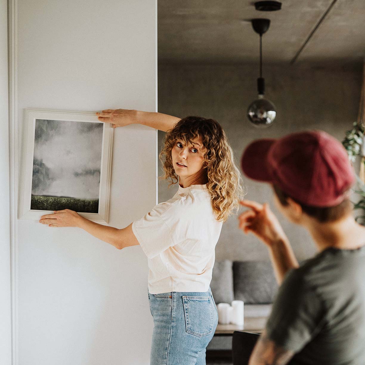 Par hænger kunst op på væggen i stue og indretter hjemmet med fokus på personlig boligindretning og ophængning af billeder
