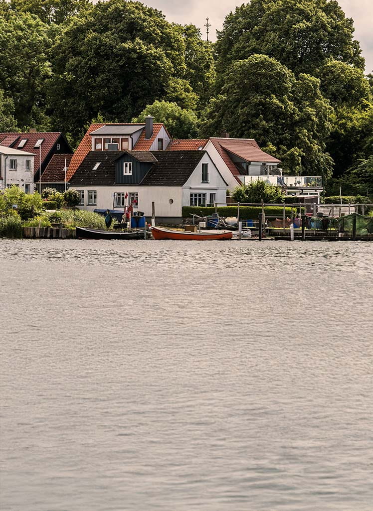 Landsby ved vand med små huse, både og grønne træer i baggrunden