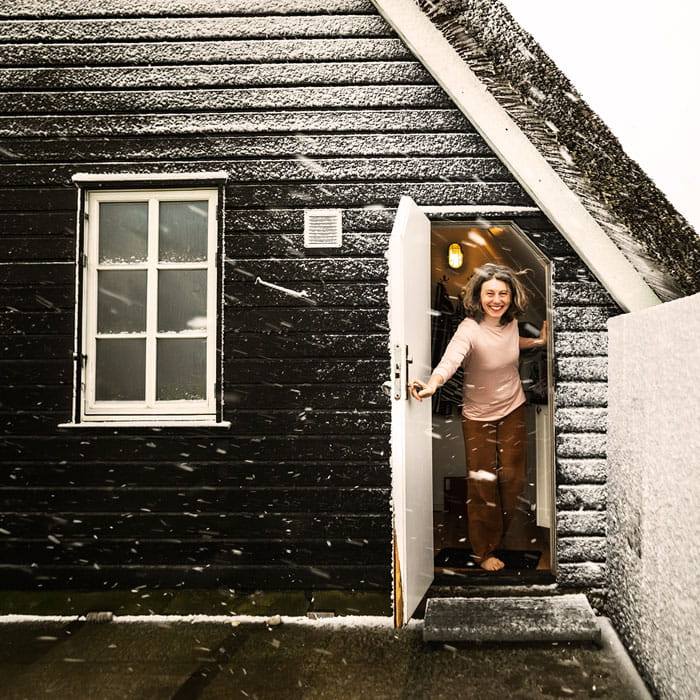 Kvinde træder ud af sommerhus i vintervejr med sne på taget, velegnet til helårsbeboelse