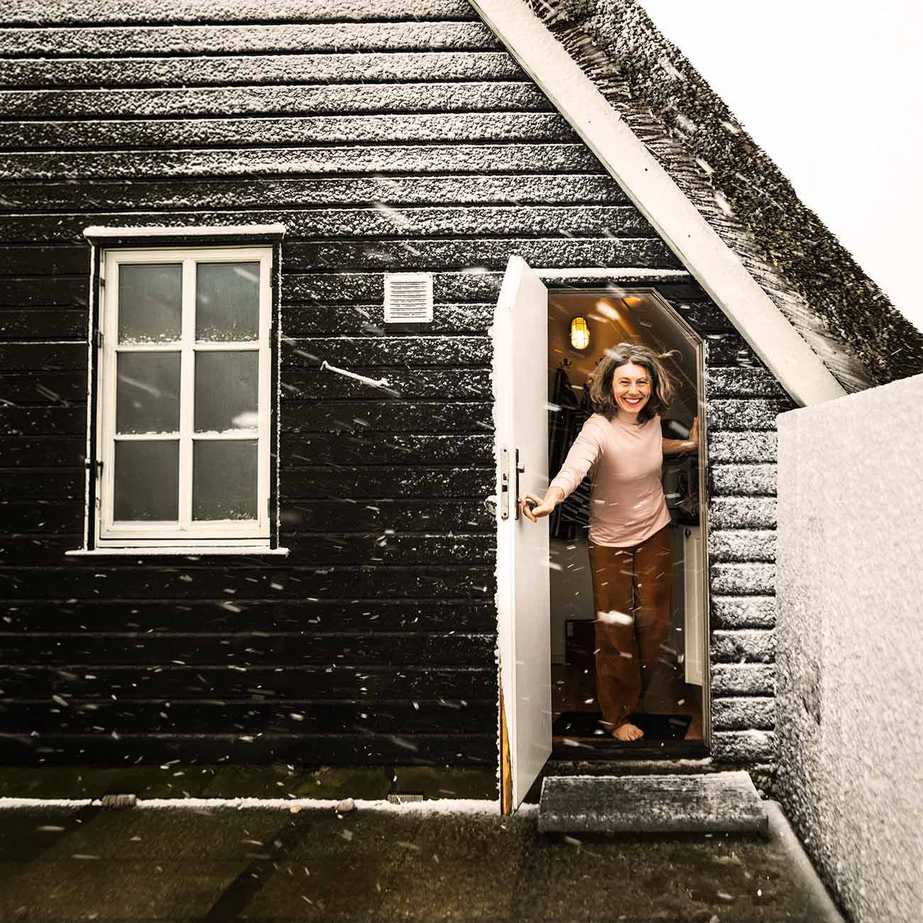Kvinde træder ud af sommerhus i vintervejr med sne på taget, velegnet til helårsbeboelse